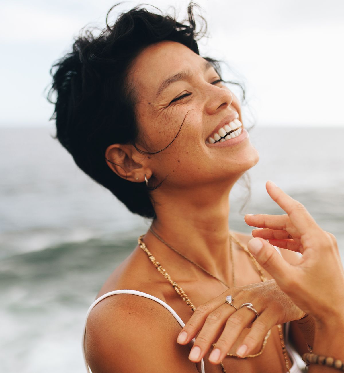 Smiling woman near the ocean, wearing jewelry.