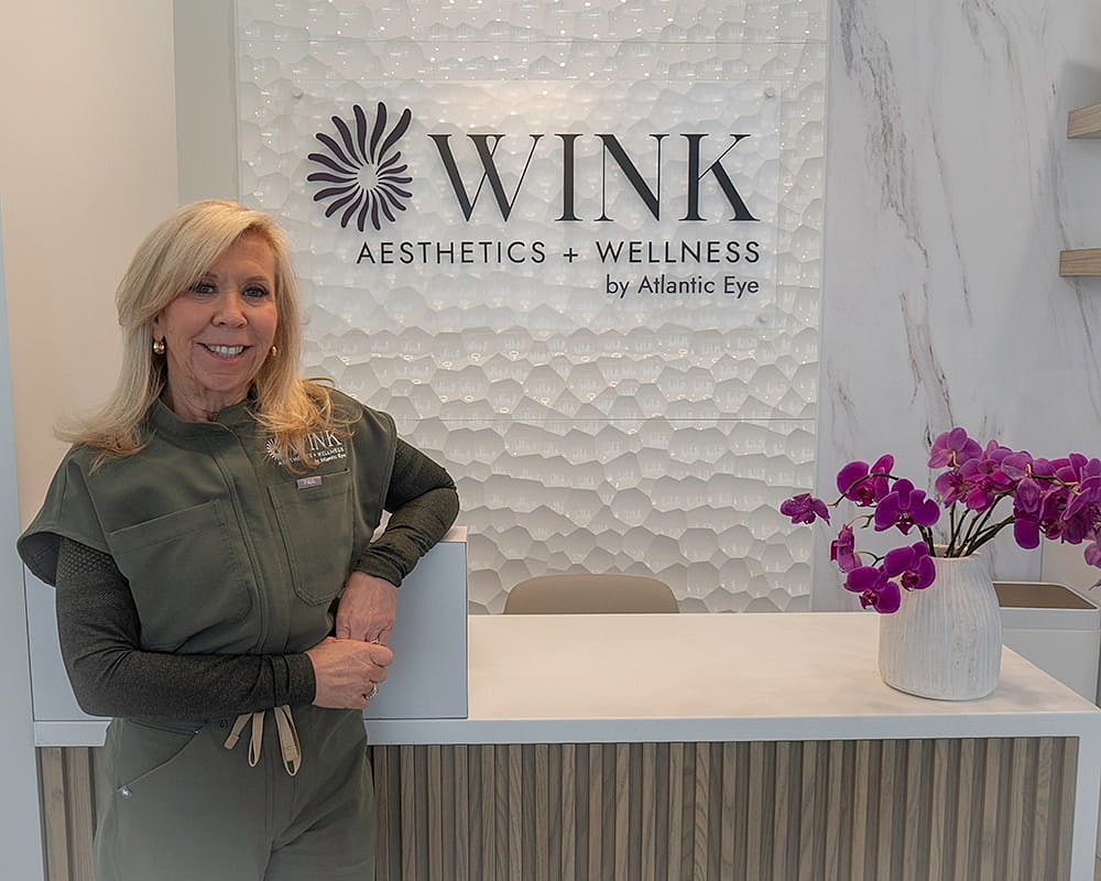 Woman smiling at WINK Aesthetics reception desk.