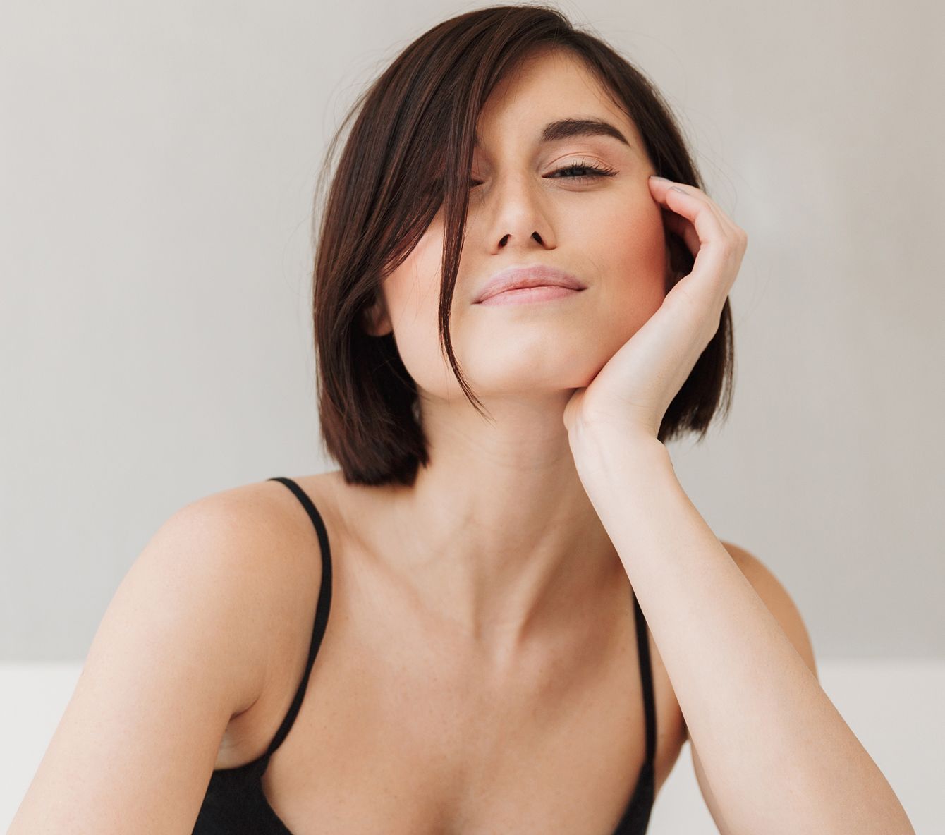 Woman smiling with hand on face, neutral background.
