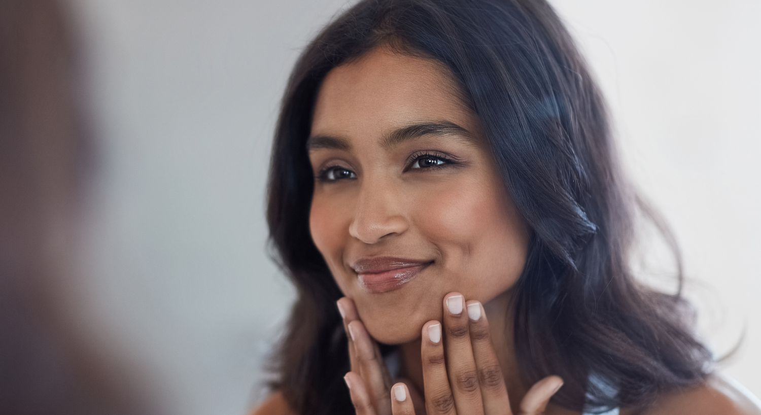 Smiling woman gently touching her face.