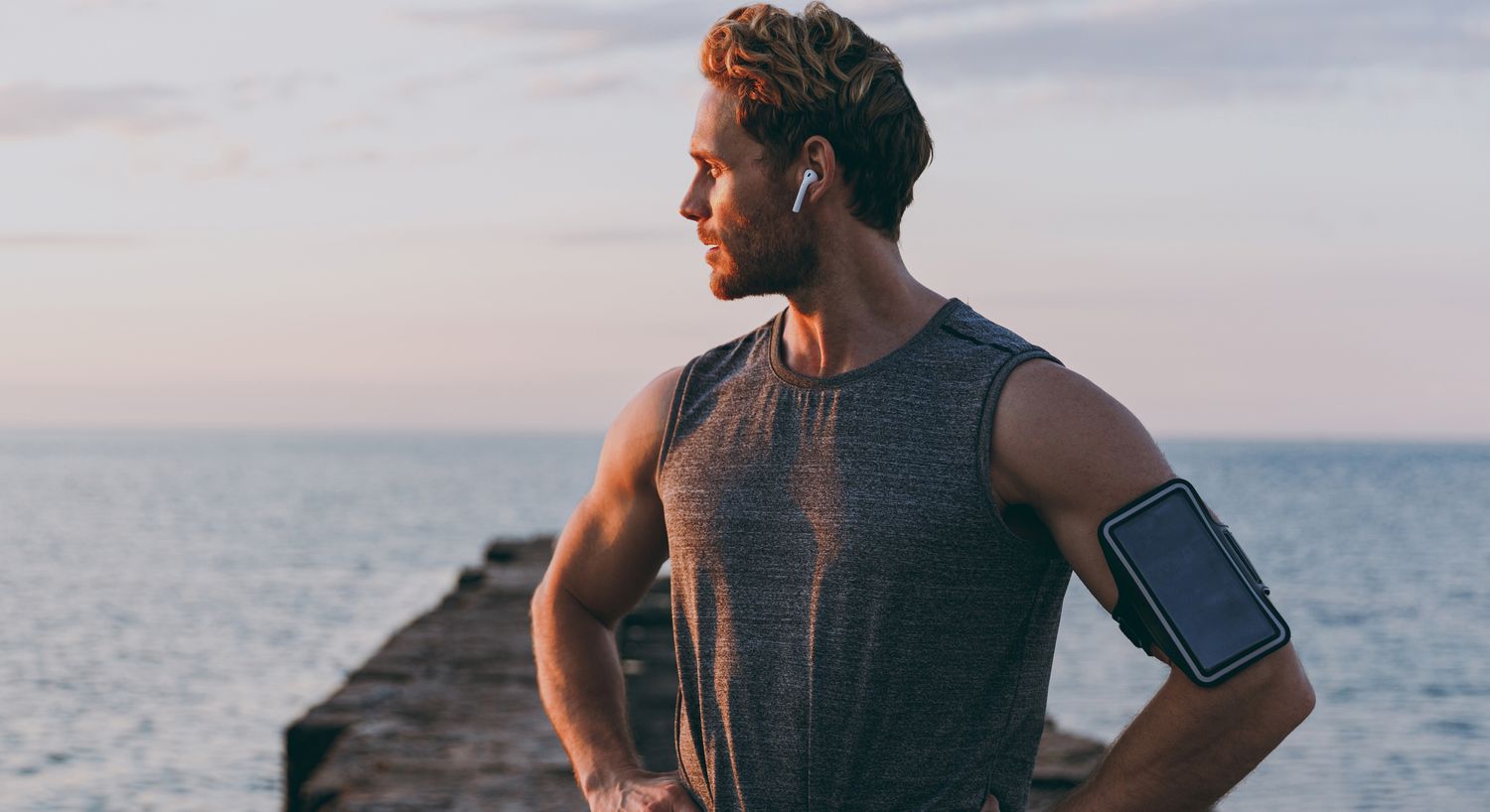 Man with headphones by the water at sunset.